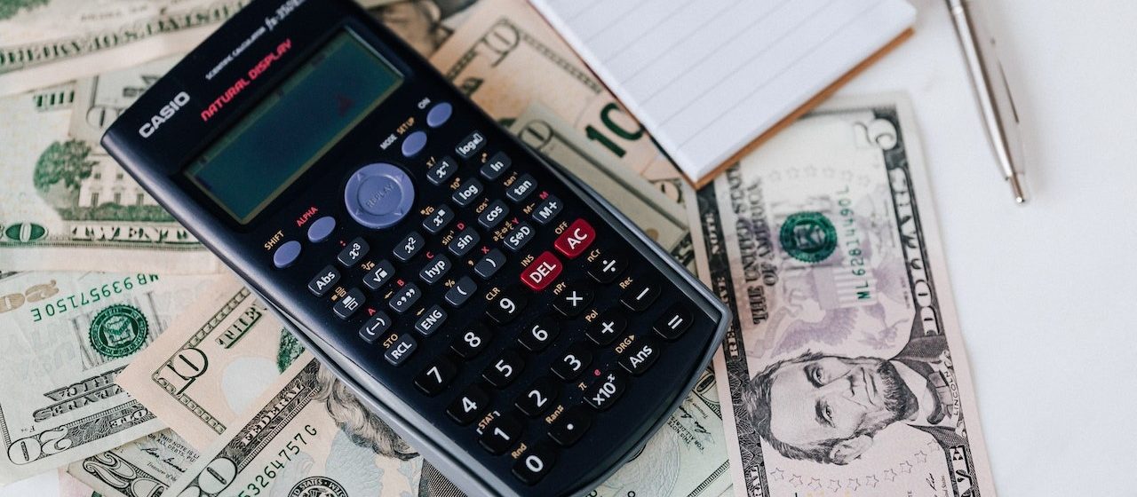 Calculator and a small book on top of a dollar bills | Breast Cancer Car Donations