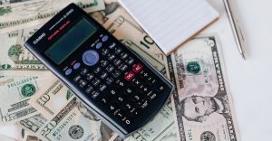 Calculator and a small book on top of a dollar bills | Breast Cancer Car Donations