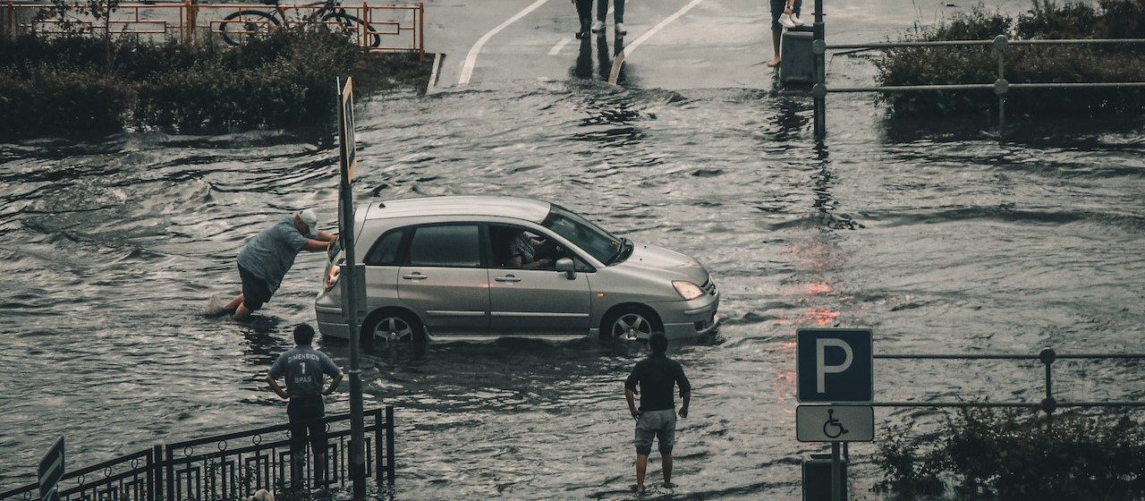 Man pushing a car on a flooded street | Breast Cancer Car Donations