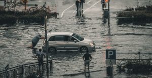 Man pushing a car on a flooded street | Breast Cancer Car Donations