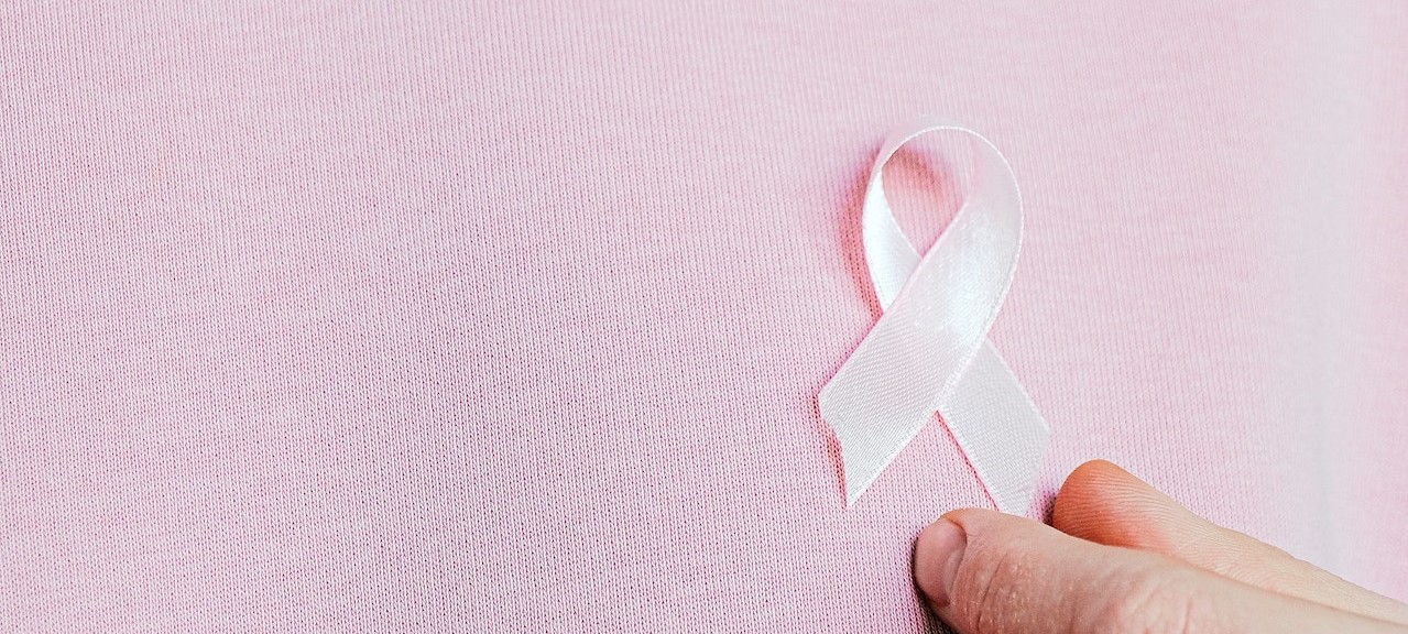 Person holding pink ribbon on his chest | Breast Cancer Car Donations