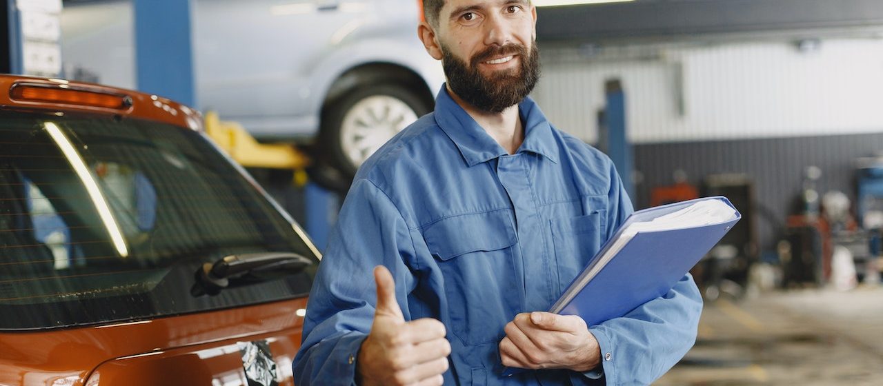 Man in Blue Coveralls Standing in an Auto Repair Shop | Breast Cancer Car Donations