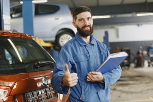 Man in Blue Coveralls Standing in an Auto Repair Shop | Breast Cancer Car Donations