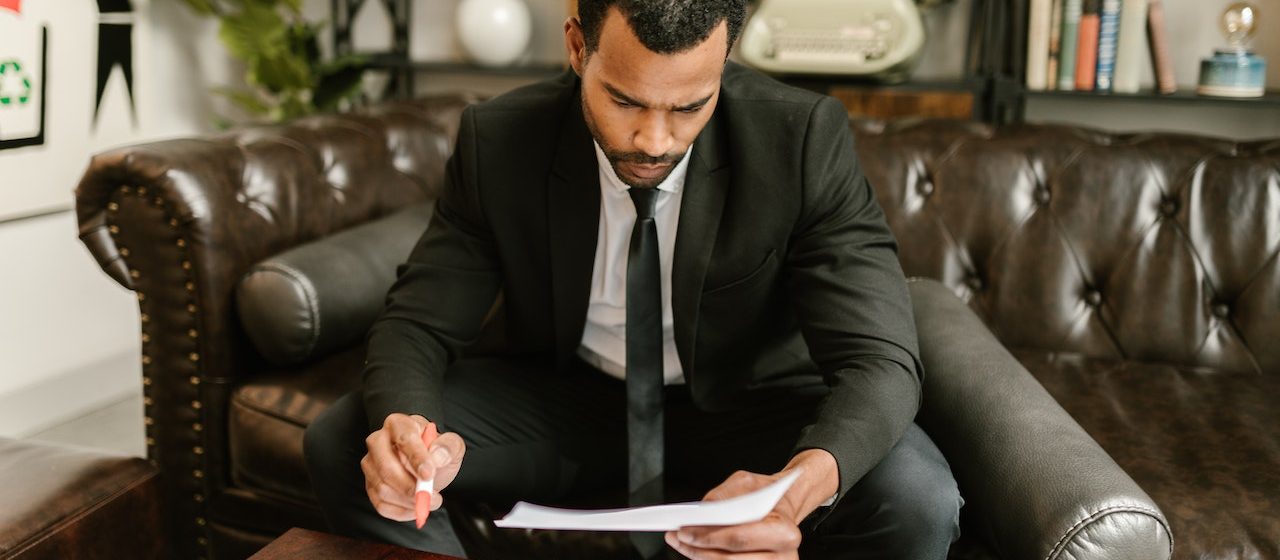 Man Sitting on Brown Leather Sofa Looking At Documents | Breast Cancer Car Donations