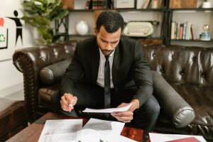 Man Sitting on Brown Leather Sofa Looking At Documents | Breast Cancer Car Donations