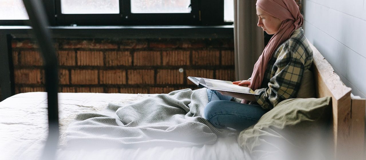 Woman Reading a Book while in Bed | Breast Cancer Car Donations