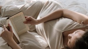 Woman Lying on Bed with Pillows Reading Book | Breast Cancer Car Donations