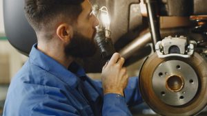 Man in Blue Coveralls Doing Inspection on Brakes of a Car | Breast Cancer Car Donations