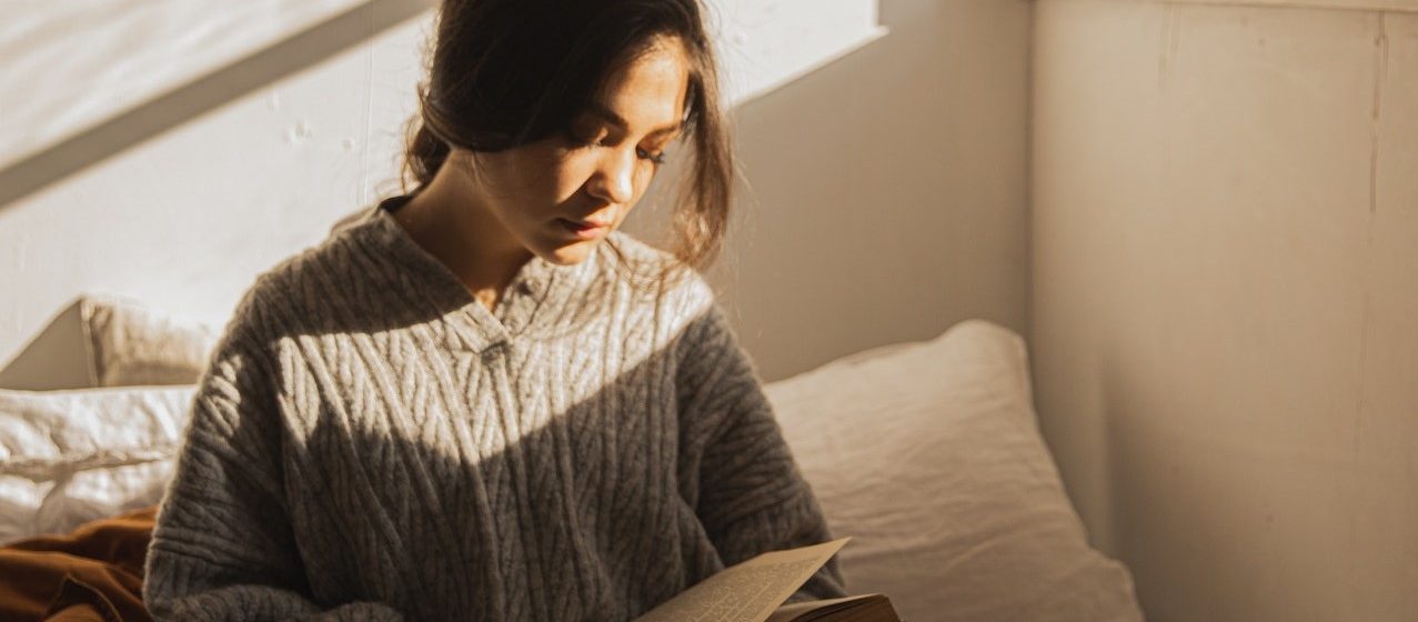 Woman in Gray Long Sleeve Shirt Sitting on Her Bed Reading a Book | Breast Cancer Car Donations