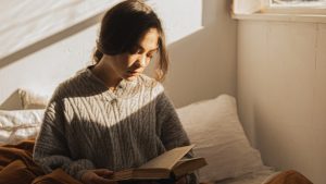 Woman in Gray Long Sleeve Shirt Sitting on Her Bed Reading a Book | Breast Cancer Car Donations
