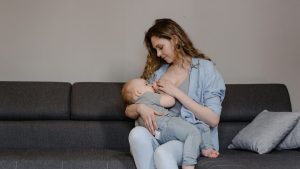 A Woman Breastfeeding Her Baby while Sitting on the Couch | Breast Cancer Car Donations