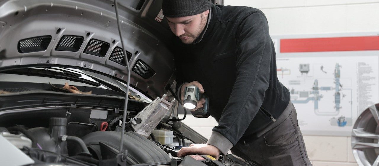 Man in Black Jacket and Black Knit Cap Inspecting Car Engine | Breast Cancer Car Donations