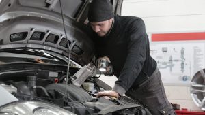 Man in Black Jacket and Black Knit Cap Inspecting Car Engine | Breast Cancer Car Donations