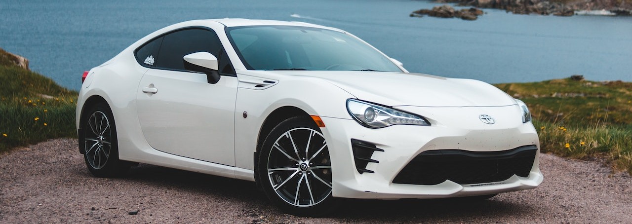 White automobile on gravel road near lake | Breast Cancer Car Donations