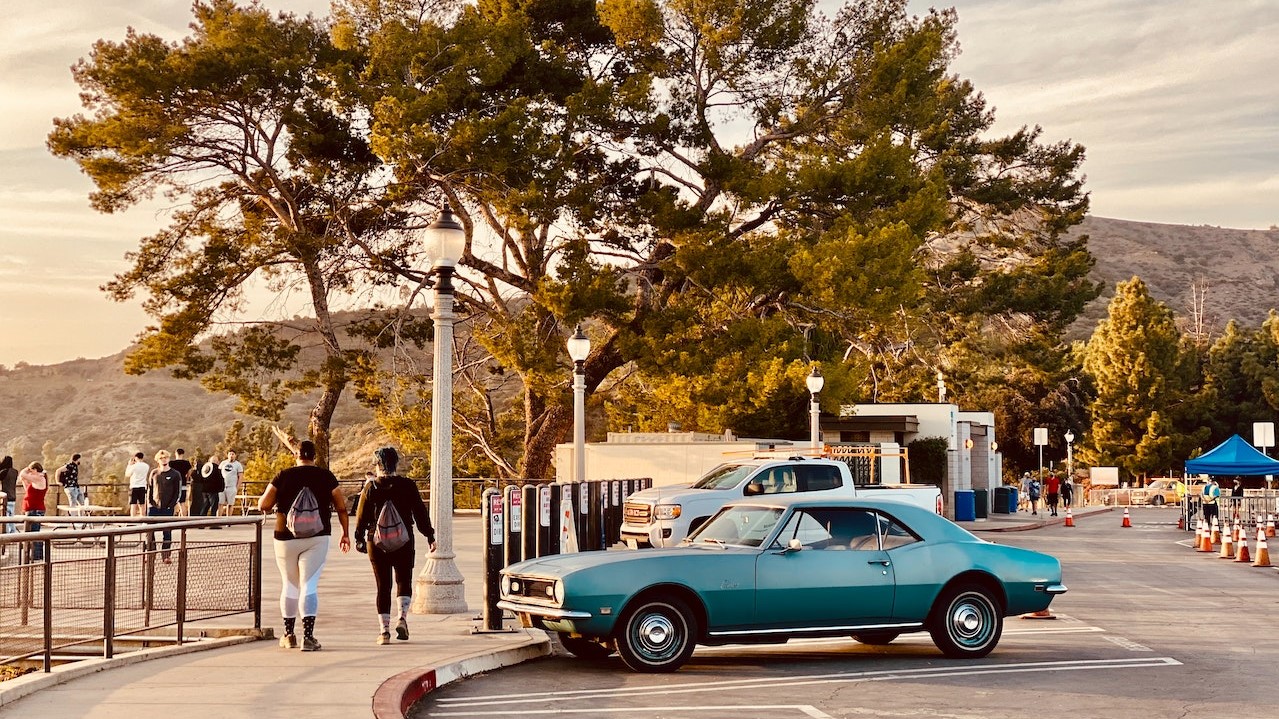 Blue Coupe on Park Near People Walking on Sidewalk | Breast Cancer Car Donations