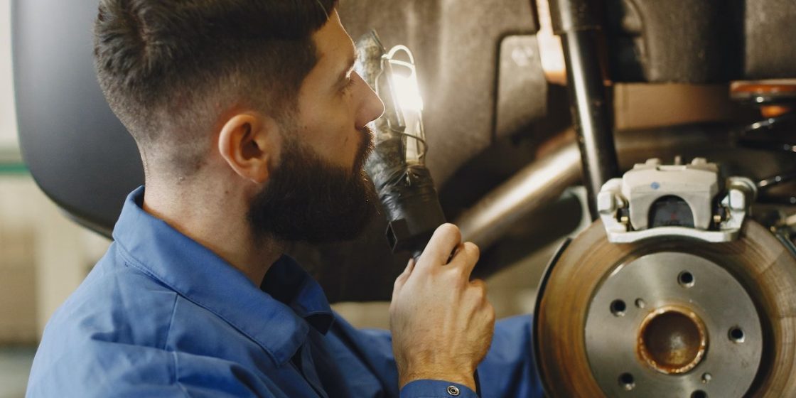 Man in Blue Coveralls Doing Inspection on Brakes of a Car | Breast Cancer Car Donations