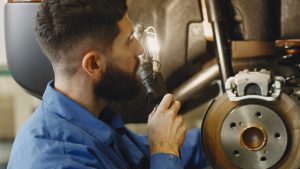 Man in Blue Coveralls Doing Inspection on Brakes of a Car | Breast Cancer Car Donations