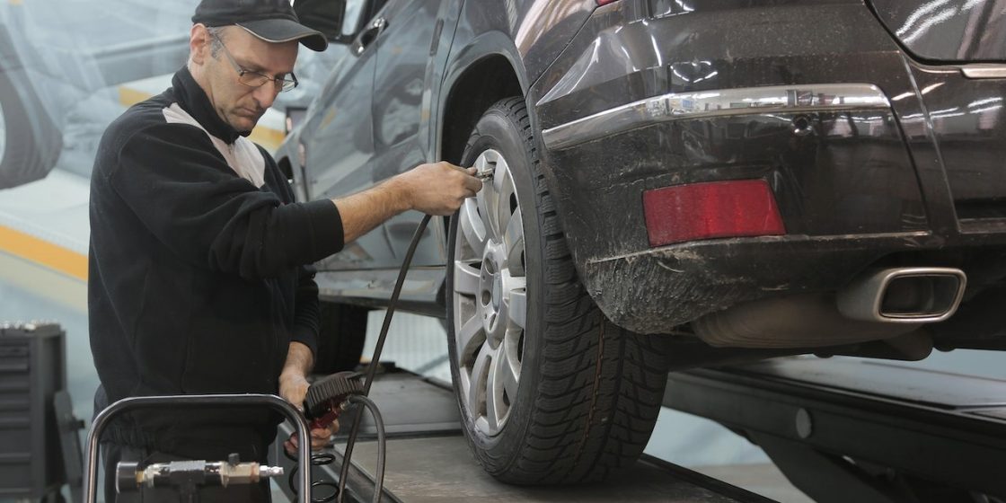 Serious car mechanic pumping up car wheel in modern service garage | Breast Cancer Car Donations