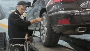Serious car mechanic pumping up car wheel in modern service garage | Breast Cancer Car Donations
