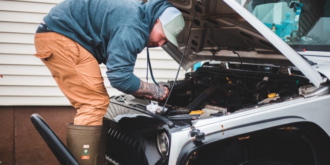 Technician repairing car engine near house | Breast Cancer Car Donations