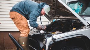 Technician repairing car engine near house | Breast Cancer Car Donations