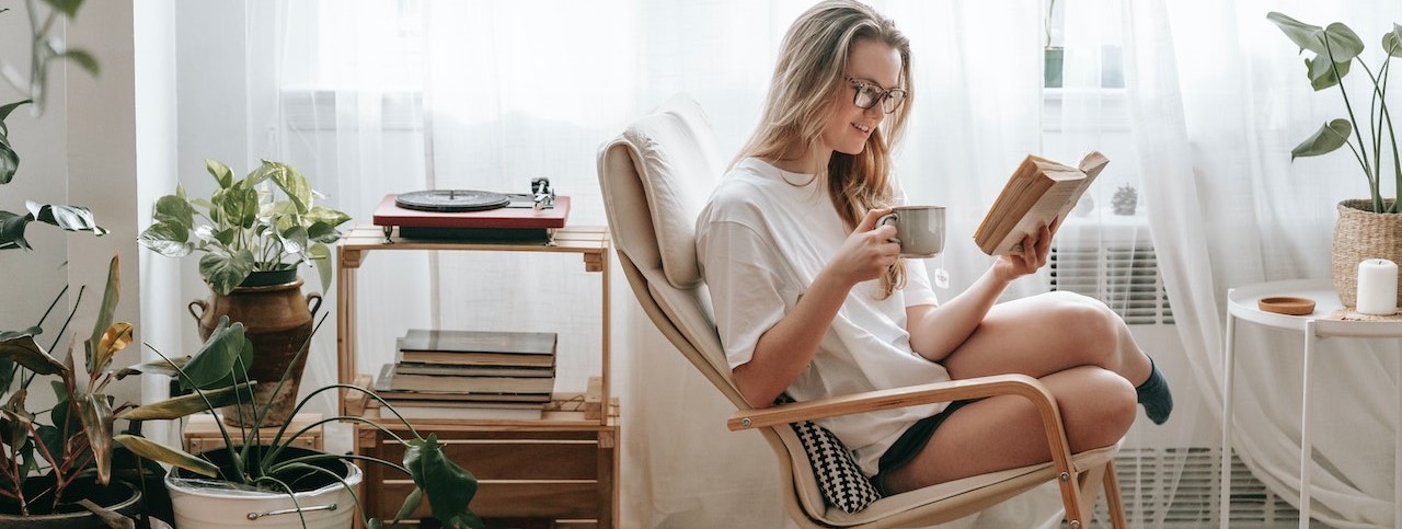 Smiling woman with hot drink reading book at home | Breast Cancer Car Donations