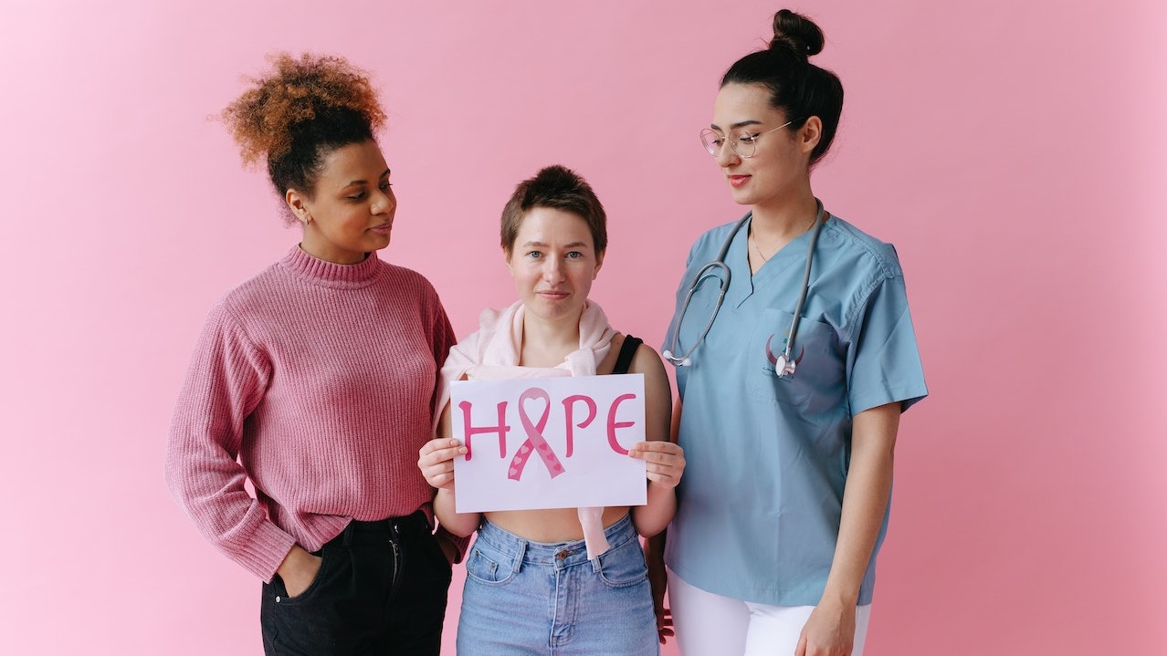 Women Looking at a Woman Holding a Placard with a Pink Ribbon | Breast Cancer Car Donations