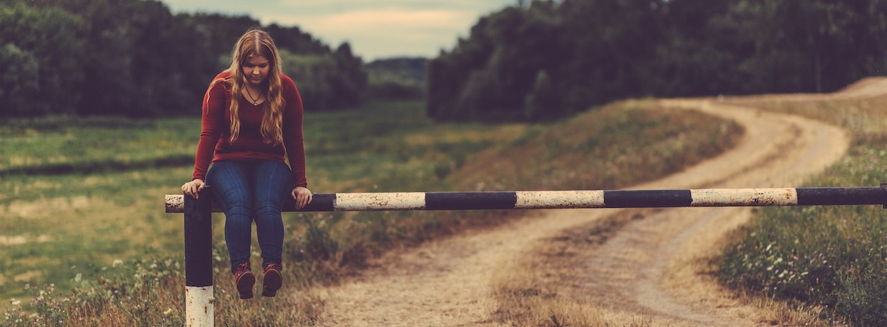 Woman Sitting on Metal Gate Pass Beside Mud Road | Breast Cancer Car Donations