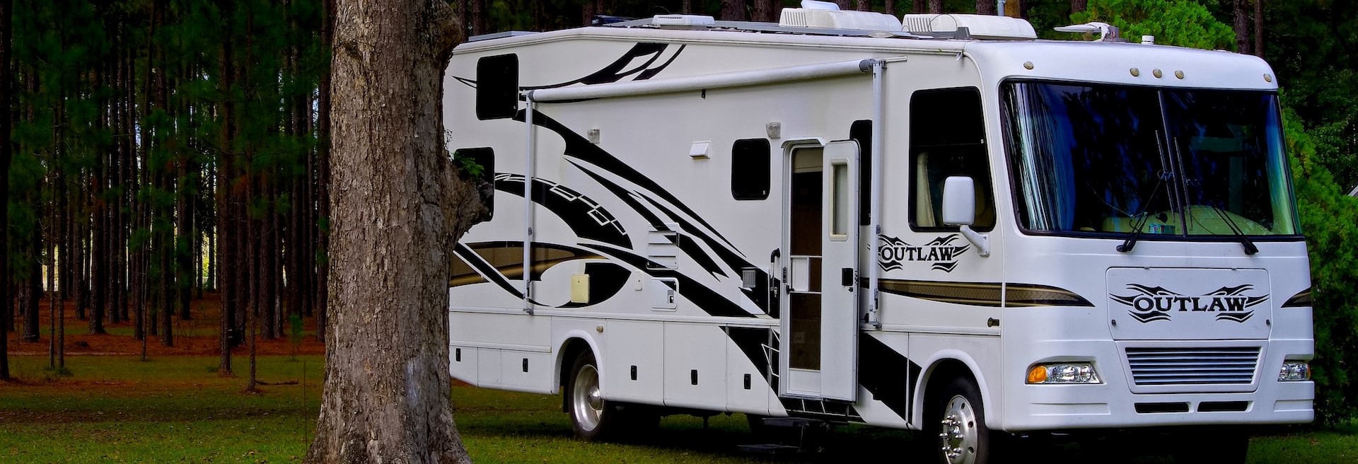 White Motorhome with a Gold and Black Lining Parked at the Forest | Breast Cancer Car Donations