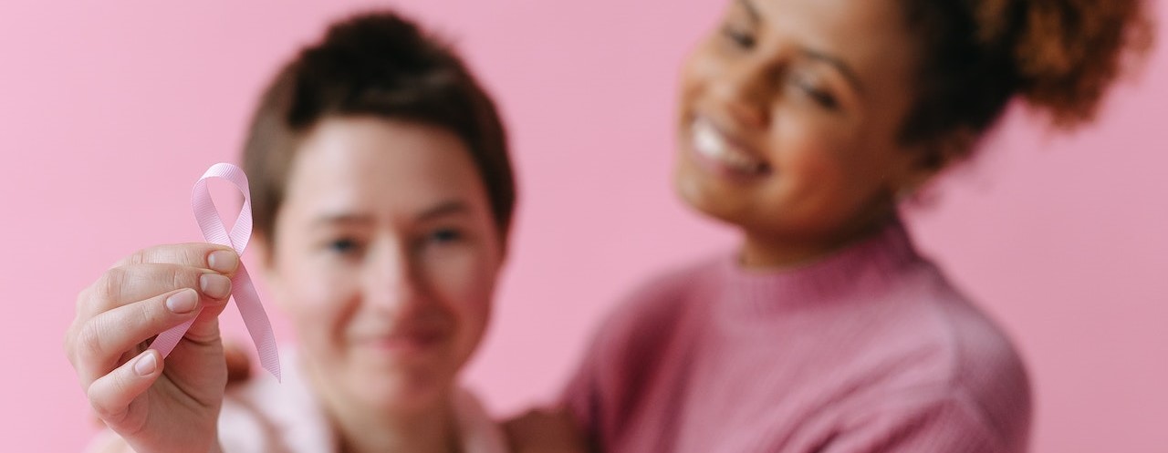 Woman holding a pink ribbon smiling | Breast Cancer Car Donations