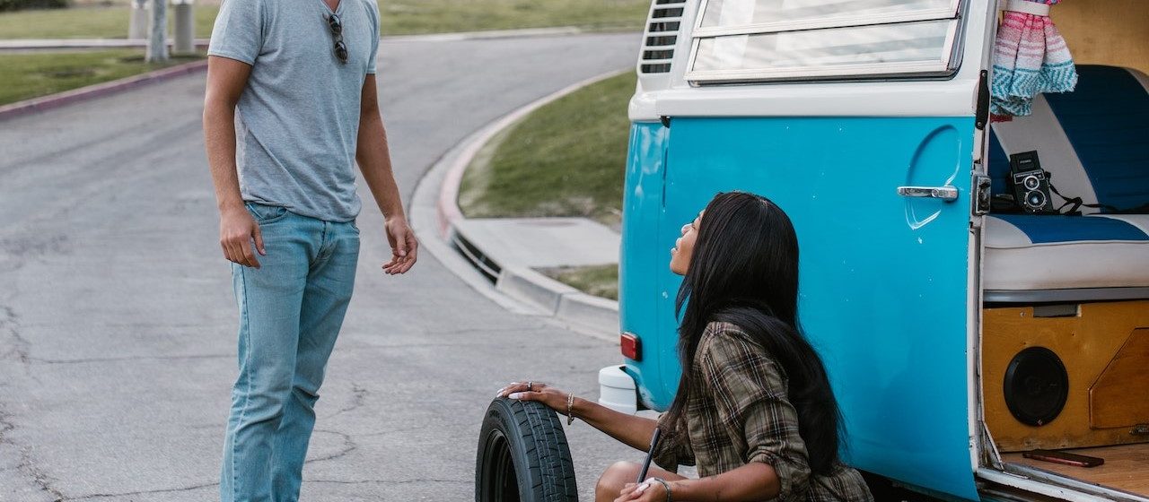 Man Talking to a Woman Changing the Tire of a Camper Van | Breast Cancer Car Donations