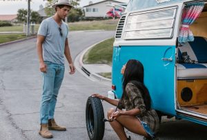Man Talking to a Woman Changing the Tire of a Camper Van | Breast Cancer Car Donations