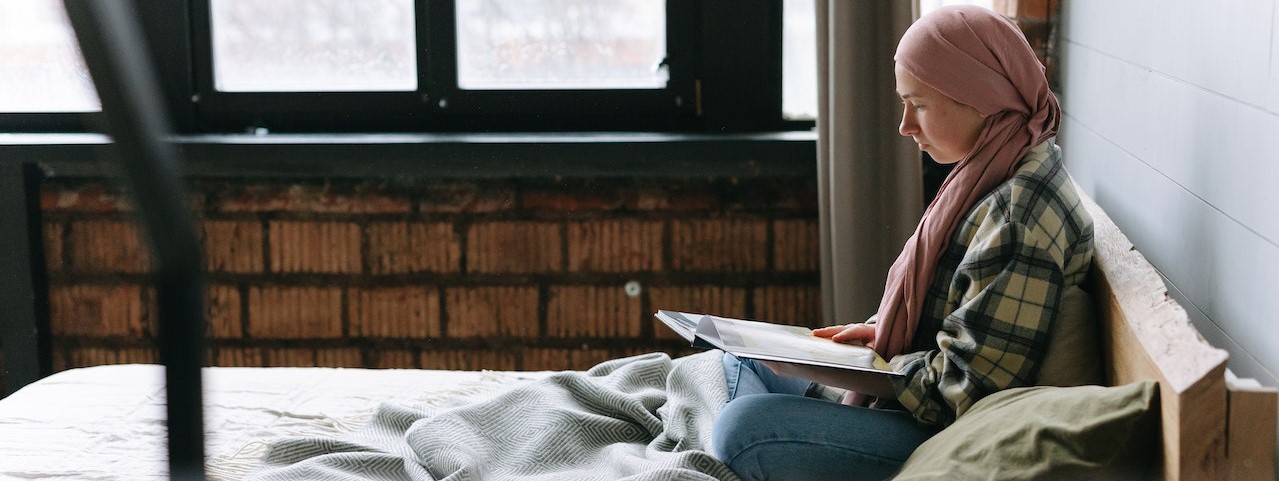 Woman Reading a Book while in Bed | Breast Cancer Car Donations