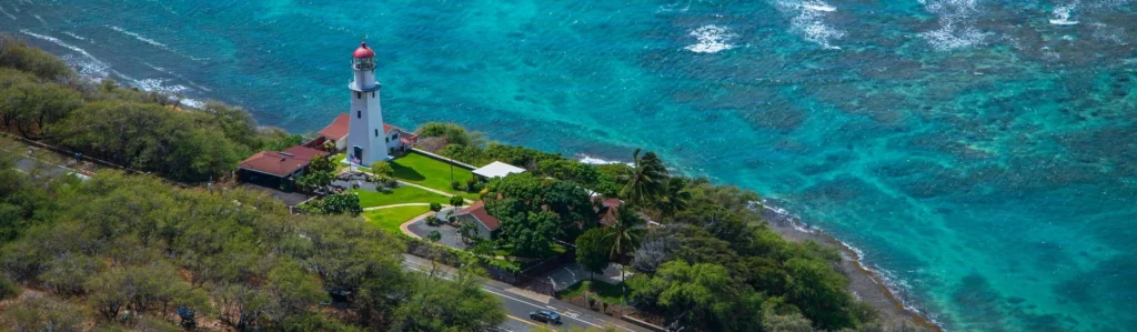 A lighthouse on a hill by the ocean with Diamond Head Lighthouse in the background