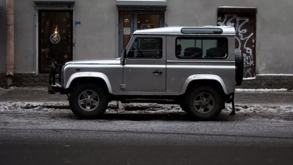 A silver SUV parked by a snowy city street near a cafe