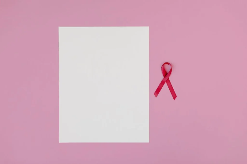 Pink background with a blank paper and a red ribbon symbolizing breast cancer awareness