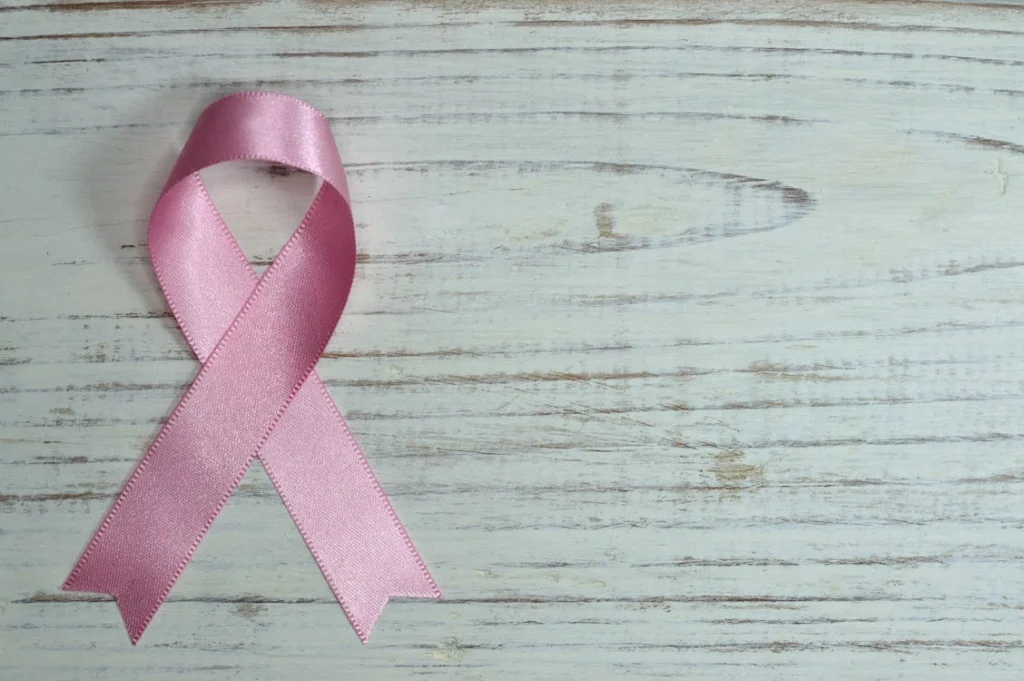 A pink ribbon symbolizing cancer awareness placed on a light wooden background