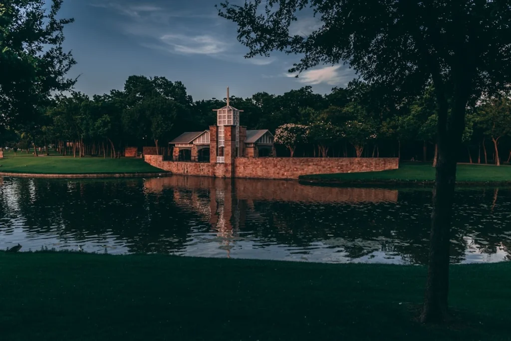 Brown concrete building near green trees and body of water during daytime