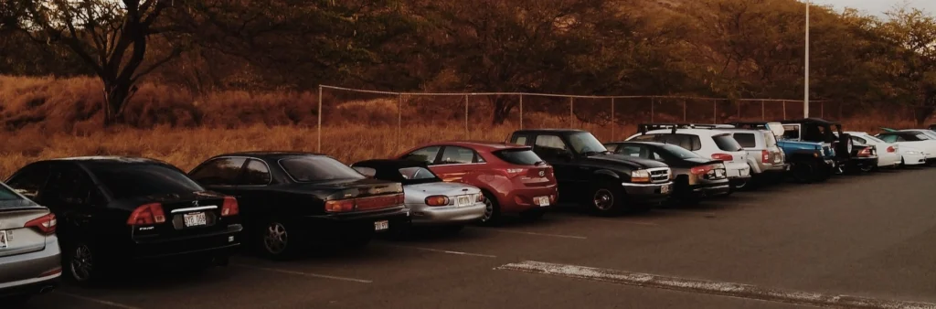 Cars parked on parking lot near brown mountain under white clouds during daytime