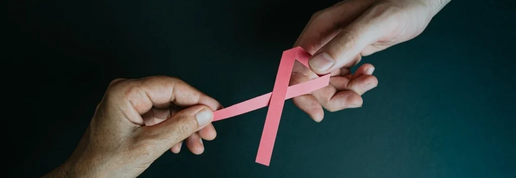 Two hands exchanging a pink ribbon symbolizing breast cancer awareness and support