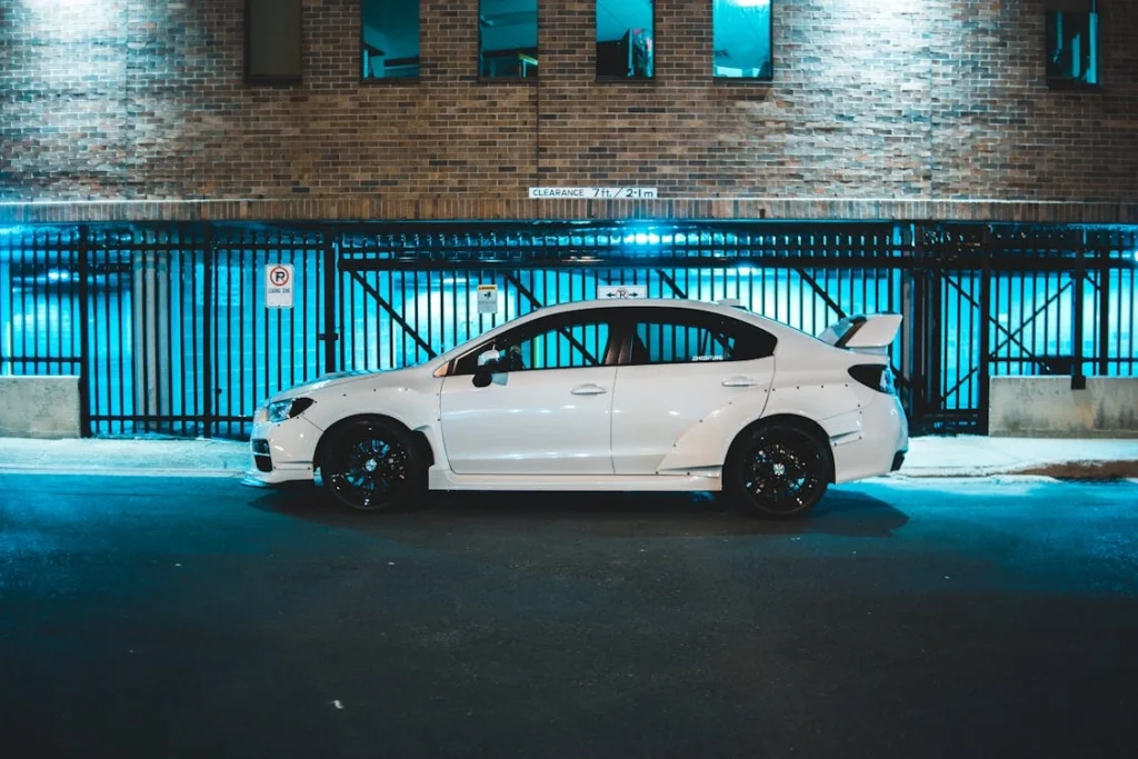 A white sports car parked on a city street at night, with a modern building background