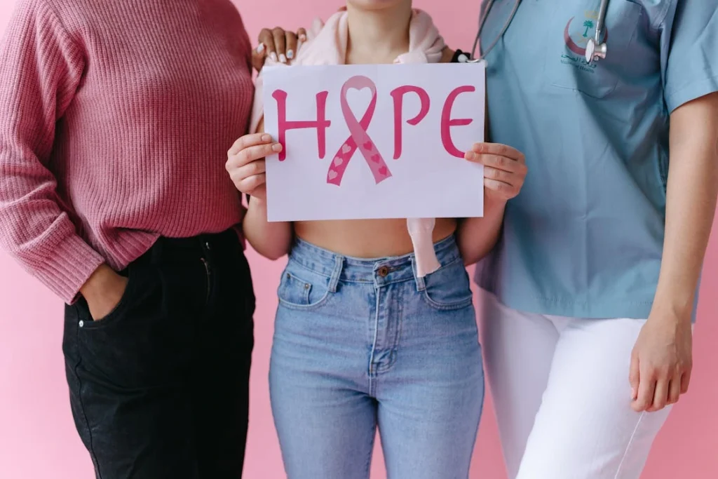 Three women holding a 'HOPE' sign with a pink ribbon for breast cancer awareness