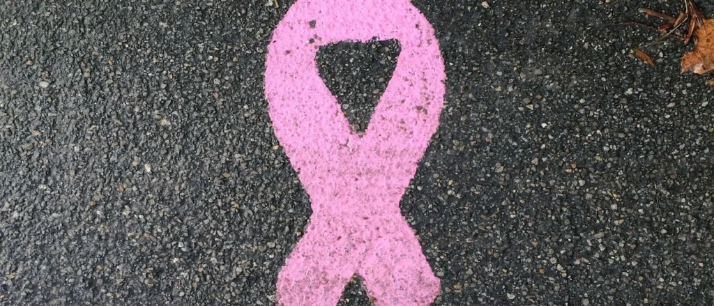 A vertical shot of feet in flip-flops next to a pink awareness ribbon on asphalt