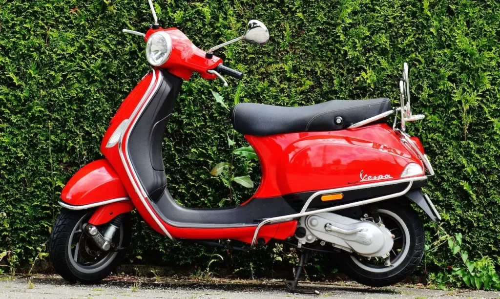 Bright red Vespa scooter parked against a lush green hedge, showcasing vibrant contrast