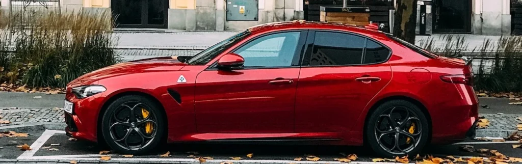 A sleek red sports car parked on a city street lined with autumn trees