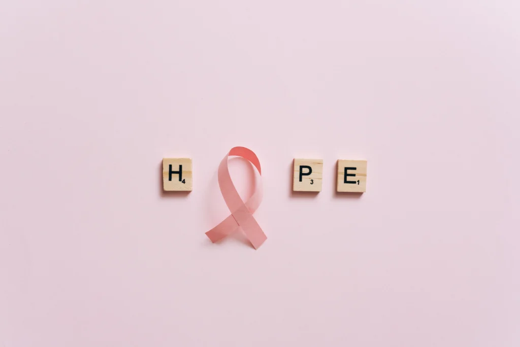 Flat lay of pink ribbon symbolizing cancer awareness with scrabble tiles spelling HOPE on a pink surface