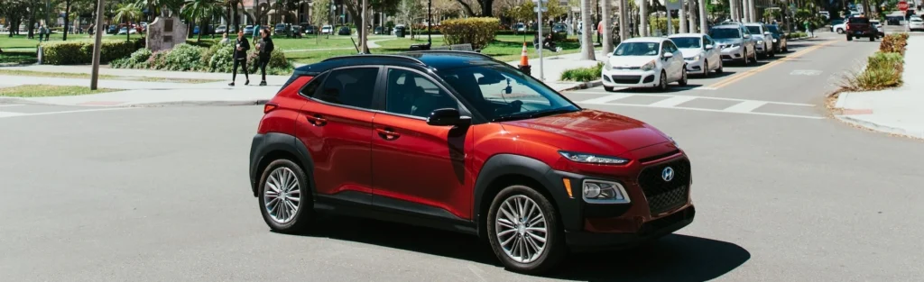 A red car driving down a street next to tall buildings