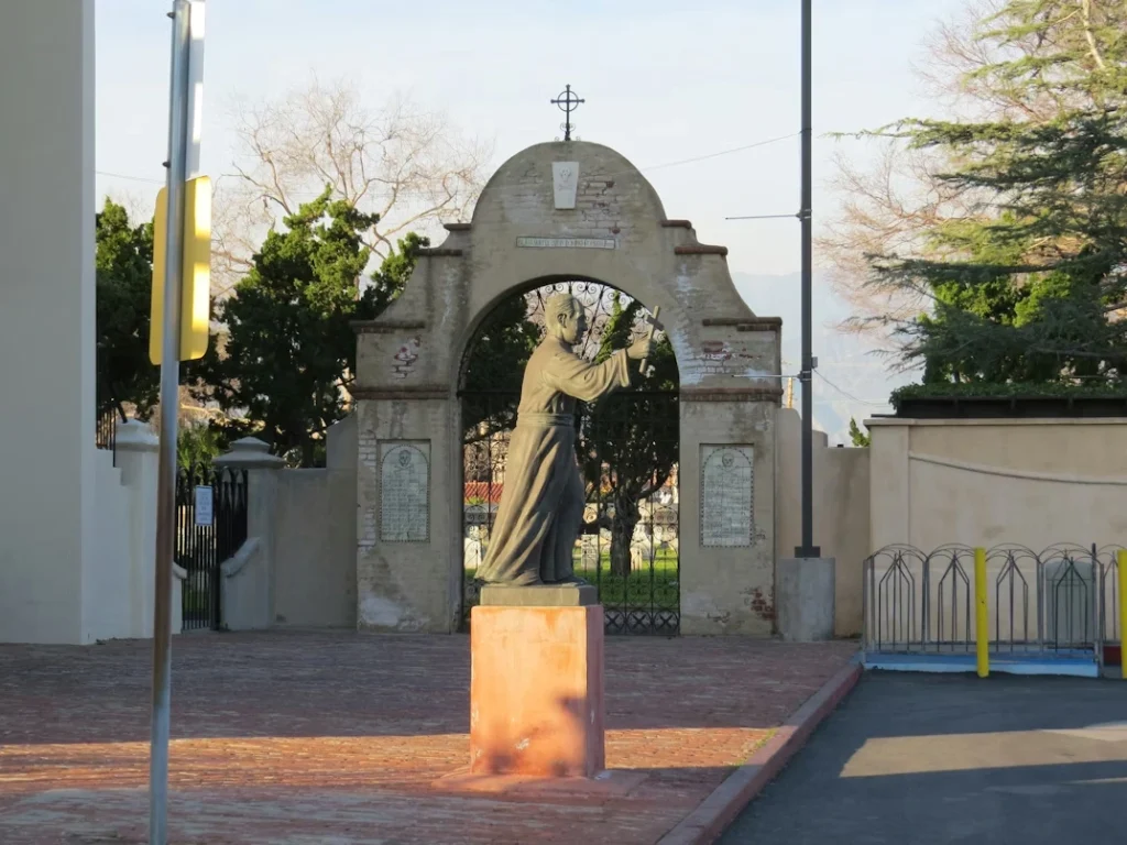A statue of a woman holding a cross in front of a gate