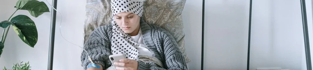 A woman undergoing chemotherapy checks her smartphone in a hospital bed, symbolizing hope and recovery