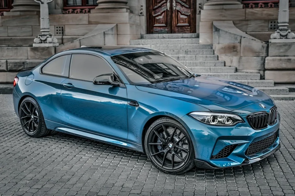 A shiny blue luxury sedan parked on a cobblestone surface in front of a grand building